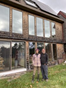Two people stand before a house with lots of windows.