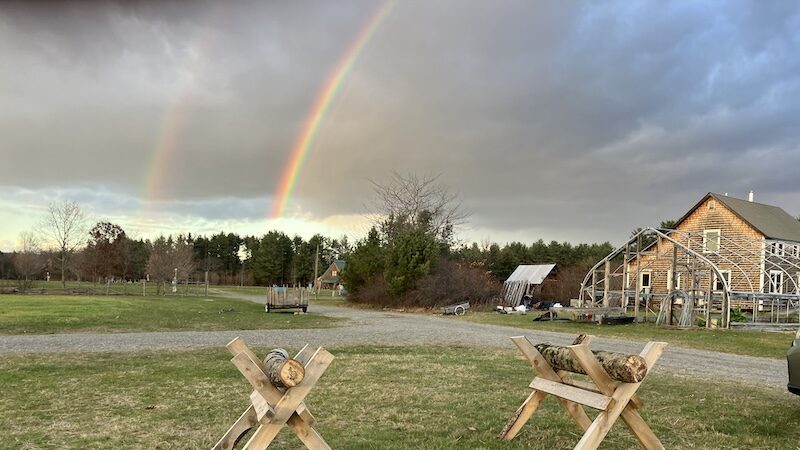 Two separate logs sitting on saw horses with two rainbows in the back.
